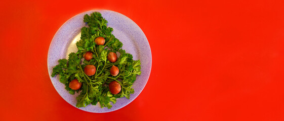 Christmas tree made of herbs and hazelnuts on a plate. New year decor from food. Isolated on a red background. Copy space