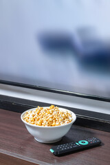 A bowl full of popcorn in front of a led tv with a remote control.