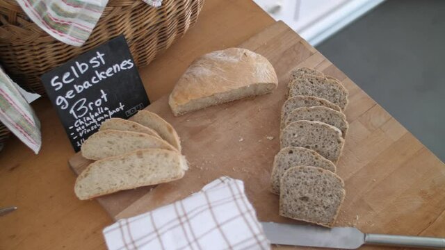 Fresh whole grain bread and white bread lying on a wooden table with a knife and a towel laying besides. Shot from above and panning camera movement. 6K Downscaled clip.