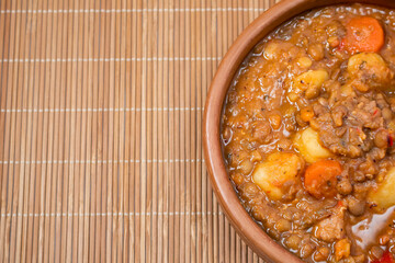 Clay bowl with homemade lentil stew, tomato, Spanish chorizo, meat and potatoes.