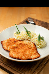 Flat, crispy golden schnitzel with beautifully served mashed potato on a wide white plate on a wooden pub table