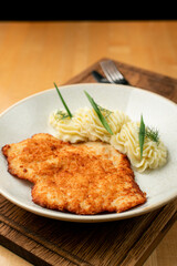 Flat, crispy golden schnitzel with beautifully served mashed potato on a wide white plate on a wooden pub table