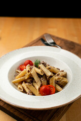 Traditional russian makarony po-flotski, also known as navy-style pasta, with ground meat and tomatoes, close up on a wooden table