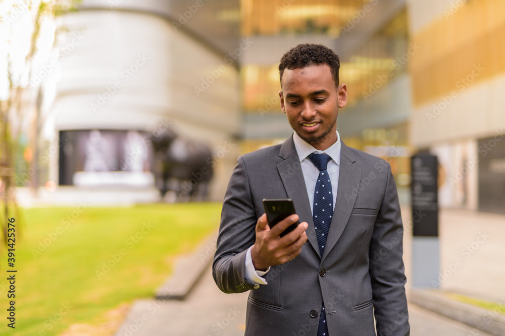 Wall mural happy african businessman outdoors smiling and using phone