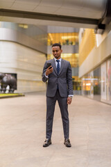 Full length shot of African businessman standing outdoors using phone