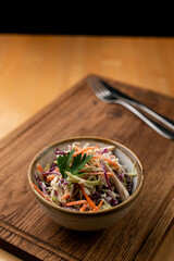 Small portion of coleslaw salad in a ceramic bowl, close up on wooden table