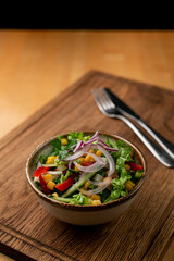 Green summer salad with corn, lettuce leaves, tomatoes and red onions, rustic style photo on wooden table