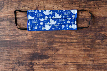 Hand made fabric masks on a wood background, celebrate Hanukkah with Jewish symbols on a blue mask
