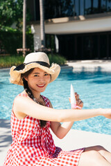 Beautiful woman in pink dress applying sunblock lotion near swimming pool.