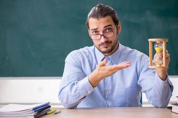 Young male teacher in the classroom in time management concept