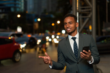 African businessman using mobile phone app waiting for taxi with hand up at night