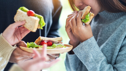 Group of young people holding and eating whole wheat sandwich in wooden plate together
