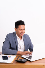 an attractive and cheerful young business man working on a laptop and smiling sitting down. On modern office desk