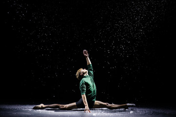 Portrait of a male dancer sitting on a twine in a dark studio against the background of falling snow.