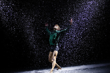 Fototapeta na wymiar The ballet dancer posing against the background of falling snow and studio light. Isolated on black background.