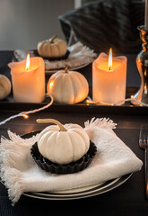 Place settings in black and white decorated with white pumpkins and white candles, vertical stock photo