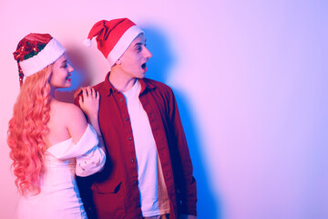 Couple in santa hats, new year, christmas. Lovers in neon light. Surprised couple looking to the side at empty space for text