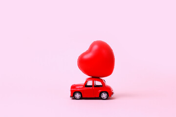 Small red retro toy car with heart on the roof on pink background. New Year, Christmas, Valentines Day, World Womans Day present delivery. Sale concept.