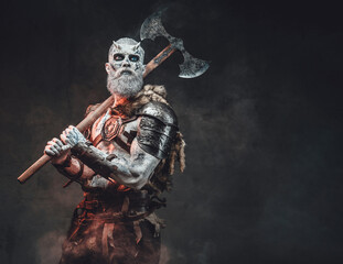 Evil and winter fashion of nordic undead warrior armed with huge two handed axe with blue eyes and pale skin in dark background.