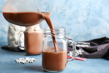 Pouring of hot cacao drink from jug into cup on color background