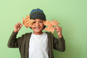 Cute African-American boy with autumn leaves on color background