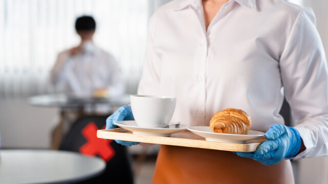 waitress wearing protective face mask and gloves for outbreak prevention Coronavirus (Covid-19) serves coffee in a restaurant, new normal and Social distancing concept.