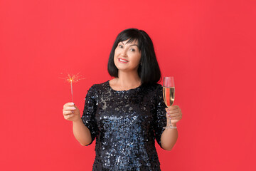 Mature woman with Christmas sparkler and champagne on color background