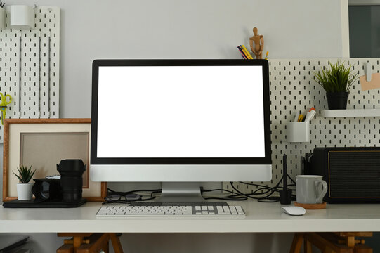 Photographer workspace with blank white desktop computer and  camera accessory. Blank screen for graphics display montage.
