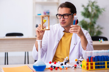 Young male chemist in time management concept
