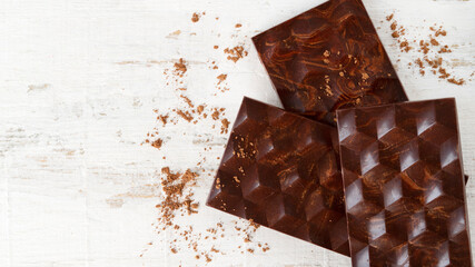Three homemade dark bitter chocolate bars with reflection on it.  Bean to bar. Cocoa powder is scattered on a light wooden background. Flat lay.