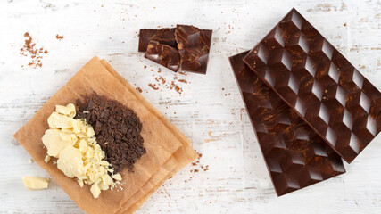 Two homemade dark bitter chocolate bars with cocoa powder in glass small bawl on white wooden background. Bean to bar. Flat lay. Horizontal orientation.