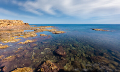 Fototapeta na wymiar The rocky coast near the eastern Spanish city of Torrevieja in autumn. There is hardly any wind. The water is clear and you can see the sea floor and the stones. A long exposure.