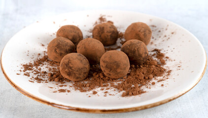 Homemade healthy vegan chocolate truffle candies with sweet cream inside. Tasty truffles on a white plate. Selective focus. Side view. Horizontal orientation.