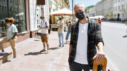 Fototapeta na wymiar Middle aged man wearing mask holding a longboard and looking at camera