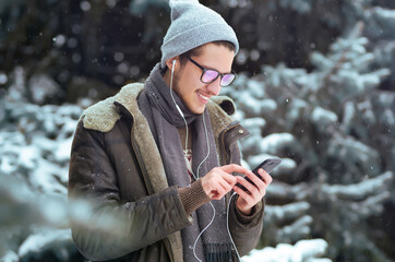 Young man with phone in winter park.  Businessman uses a phone and  enjoying winter moments in a snowy forest. Snowfall.
