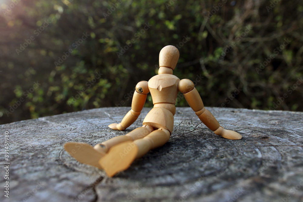 Wall mural close up of a wooden mannequin sitting outside on a tree trunk relaxing in quiet lonely forest