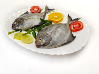Black Pomfret Decorated with Vegetables and Herbs.on a white plate.