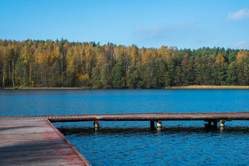A wooden footbridge in a beach. Masurian Region, Poland, Jeriozo Pluszne Małe Lake. The water reflects the colors of the sky while the trees on the bank present various colors of autumn. © juste.dcv