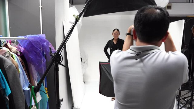 Professional photographer in a studio session with a young Asian model posing in business attire