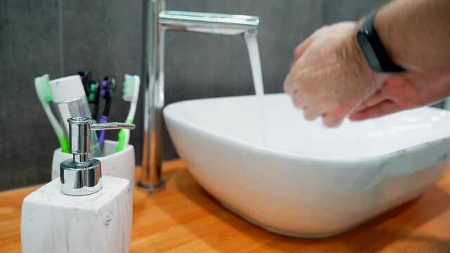 A man squeezes out liquid soap from a dispenser. Person Rinsing Hands in Bathroom at Home.