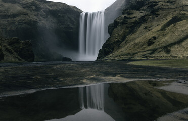 Moody dramatic long-exposure of mystical Skogafoss waterfall and reflection in southern Iceland in early spring
