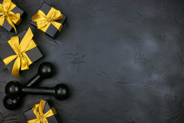A pair of dumbbells and gifts with gold ribbons on a black background.  Holiday fitness sale or black friday concept.