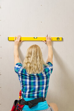 DIY blond young attractive woman using spirit level to work out measurements on plasterboard wall.