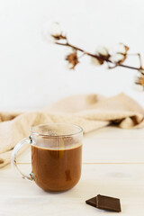Hot chocolate with coconut milk and carob in a glass mug on a white table.