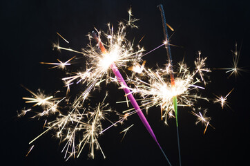 Two sparklers are lit, on a black background