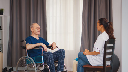 Old man in wheelchair talking with doctor. Disabled disability old person with medical worker in nursing care home assistance, healthcare and medicine service
