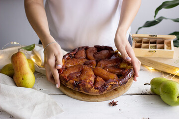 Pear tart Tatin with caramel. Female hands holding a pie.