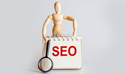 Wooden man shows with a hand to white notepad with text SEO
