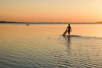 Fototapeta premium Girl silhouette on a background of sunset. The girl walks in shallow water with an inflatable circle. Copy space. 