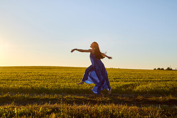 Beautiful woman or girl with magnificent figure and plastic movements walking and dancing in green field with trimmed grass in the setting sun during sunset with warm yellow light.